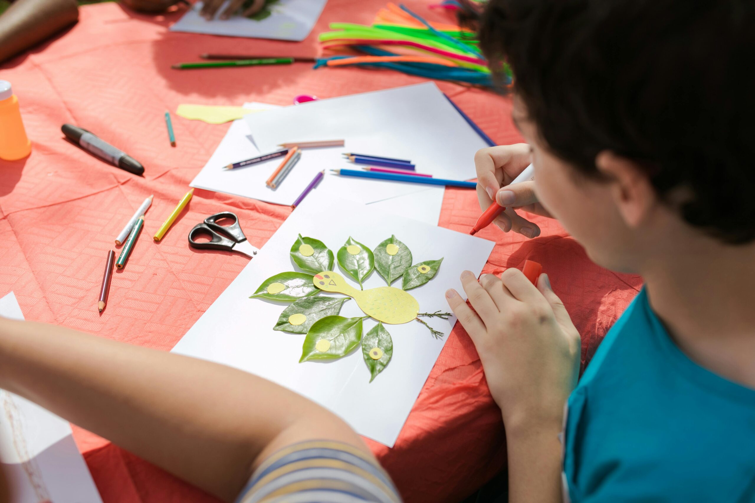 Child creating an art piece using leaves and crayons during a craft session outdoors.